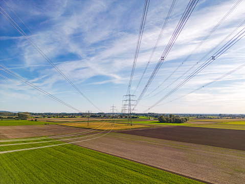 Rural nature landscape in conflict with artificial structures of power poles and power lines for energy for the consumer society as aerial shot