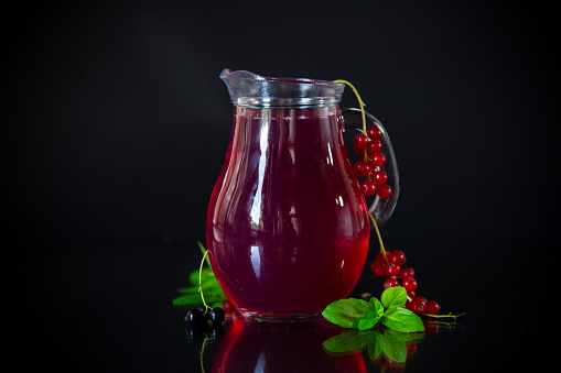 Cold refreshing drink from fresh summer berries in a decanter, isolated on a black background.