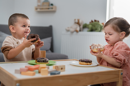 Two toddlers eating donuts at home, kids eating sugar concept