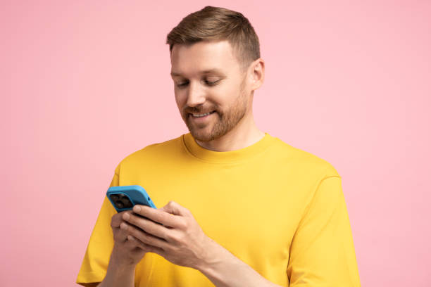 istock Smiling man looking at smartphone screen, browsing in internet chatting with friends over pink wall 1715385957