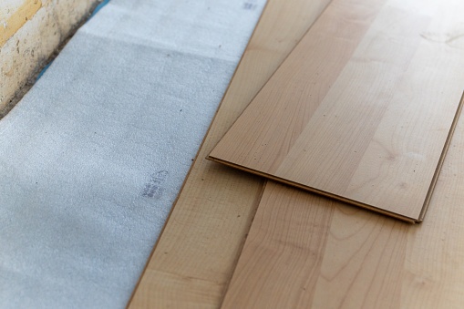 A close up portrait of stacked imitation wood laminate floorboards lying on some sound isolation ready to be installed to create a wooden floor in a house on a screed floor.
