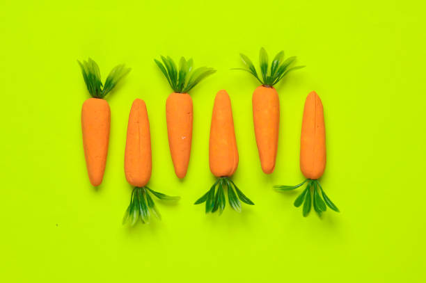 istock Plastic miniature carrot on a green background. Minimal, conceptual food still life, creative layout 1715399823