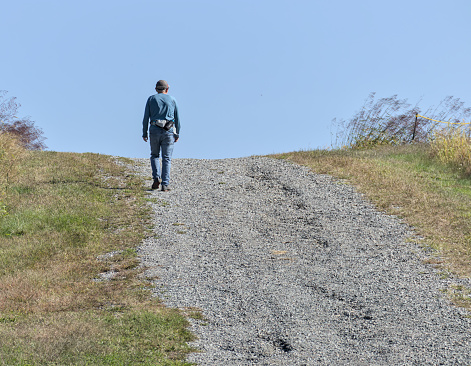 Croton on Hudson, NY - 10/01/2023: older man walking on a gravel path up a hill (hiking, recreation, adventure) elderly, mature adult, photo from behind, unrecognizable