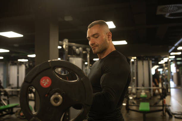 istock Muscular man training in gym doing exercises with barbell at biceps. 1715451504