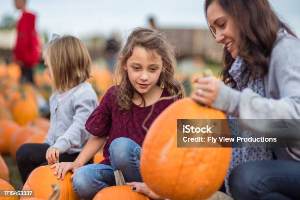 Mom And Young Daughters Examine Pumpkins At A Farm Stock Photo - Download Image Now - Day, Pumpkin, 2-3 Years