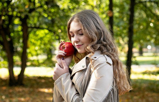 young girl with long blond hair in an autumn park with apple in her hands