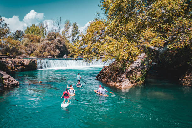 A group of white people floating on a supboard around the waterfall in the river