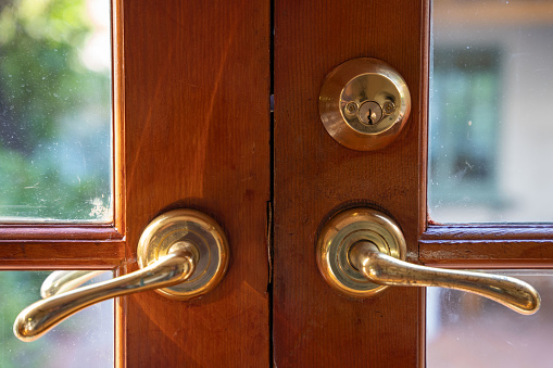 Close up on two brass door handles on a wooden door with window panes.