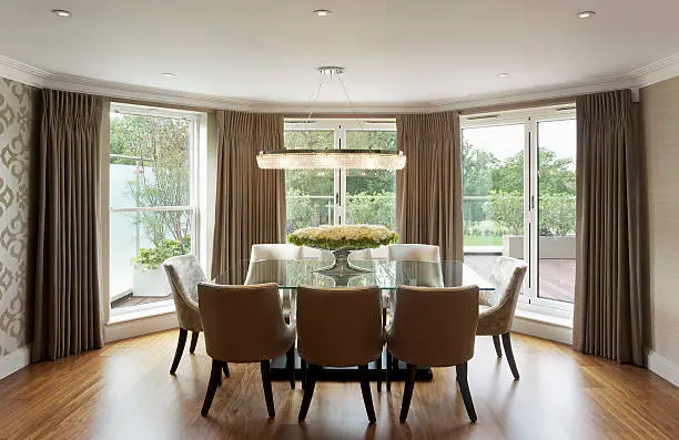 "a dining table in a luxury apartment set in a bay window with views over the large decking area and gardens. A large glass table with a black base and eight upholstered chairs sits in the centre, on a beautifully finished wooden floor.Looking for a Kitchen, Dining Room or dining related image Then please see my other images by clicking on the Lightbox link below..."