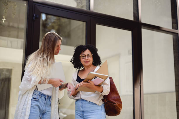 istock two female college students looking at workbook outdoors. 1715552916