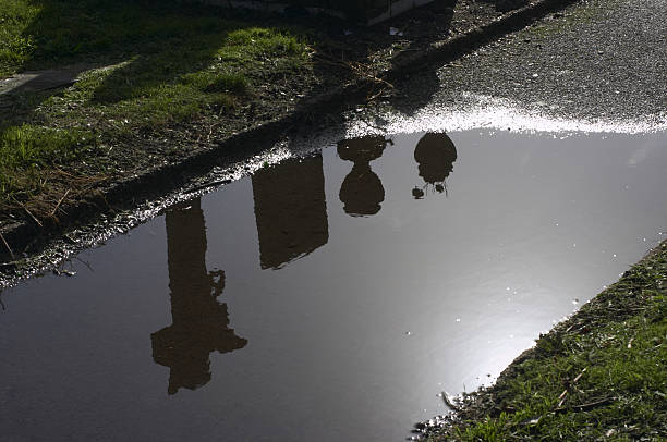 Graveyard cemetery dark reflections Sombre scene in the cemetery. Headstone, cross and urns reflected in a puddle left by a recent storm. tombstone rain cross shape cross stock pictures, royalty-free photos & images