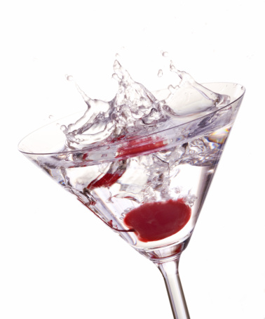 A red cherry splashing into a cocktail glass