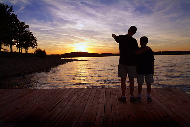 Father and Son Standing on a Boat Dock at Sunset stock photo