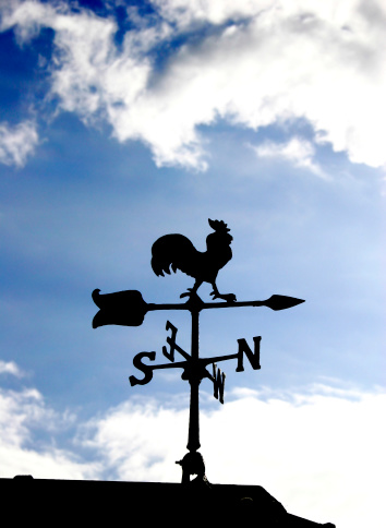 A weathercock shiloetted against a bright blue sky.