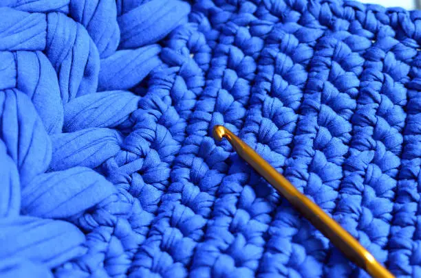Blue crocheted pattern with a crochet hook, hobby inspiration, crocheted texture background, handmade design