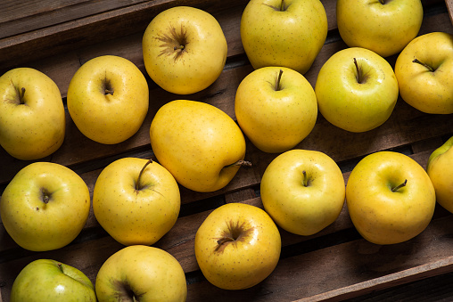 Fresh yellow apples in a wooden package on a wooden background