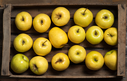 Fresh yellow apples in a wooden package on a wooden background