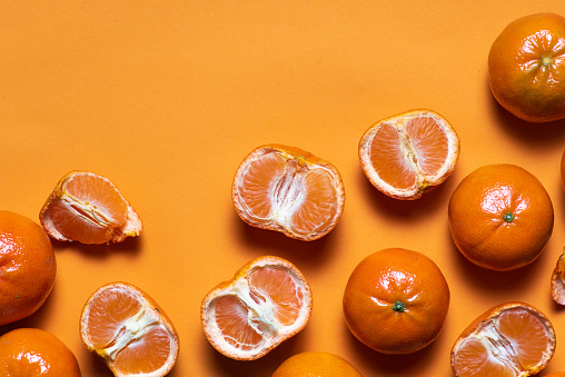Fresh whole and sliced tangerines on an orange background