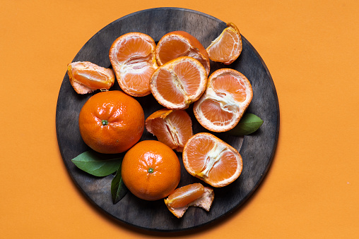 Fresh whole and sliced tangerines on a wooden board and orange background.Top view