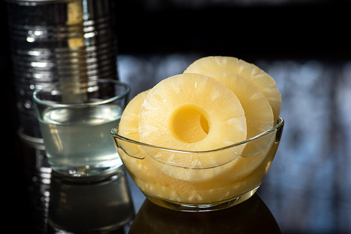 Slices of pineapple in a glass bowl on a dark background