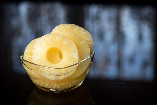 Slices of pineapple in a glass bowl on a dark background