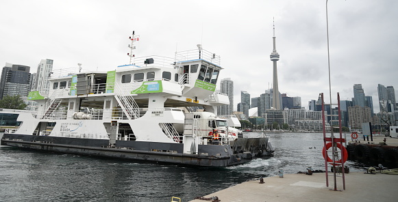 Toronto, Canada - August 25, 2023: The Island Airport Ferry sails south from Bathurst Quay across the Western Channel to Billy Bishop Toronto City Airport. Looking north from Centre Island to the Harbourfront-CityPlace neighbourhood. Overcast sky in summer.