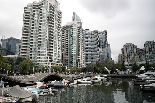Toronto, Canada - August 25, 2023: Upscale buildings and marinas line the Habourfront neighbourhood at the Inner Harbour. The Toronto Wavedecks, designed by West 8 + DTAH, pass over the slips.