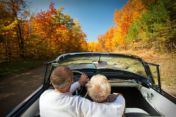 Retired couple enjoying a mid-day drive in a pink convertible on a beautiful Autumn day.