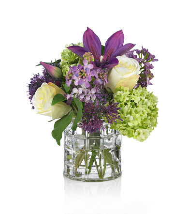 A beautiful springtime arrangement of flowers in a windowpane glass vase. The bouquet contains roses, clematis, hydrangea and lilac. Shot against a bright white background. There is a path which may be used to delete the reflection if desired. Extremely high quality faux flowers.
