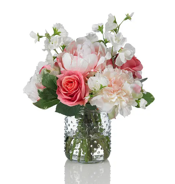 A beautiful springtime arrangement of flowers in a hobnail glass jar. The bouquet contains roses, peonies, and sweet peas. Shot against a bright white background. There is a path which may be used to delete the reflection if desired. Extremely high quality faux flowers.