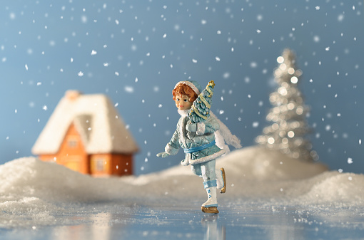Girl skates against the winter landscape with house and cristmas tree, arrangement of Christmas baubles.