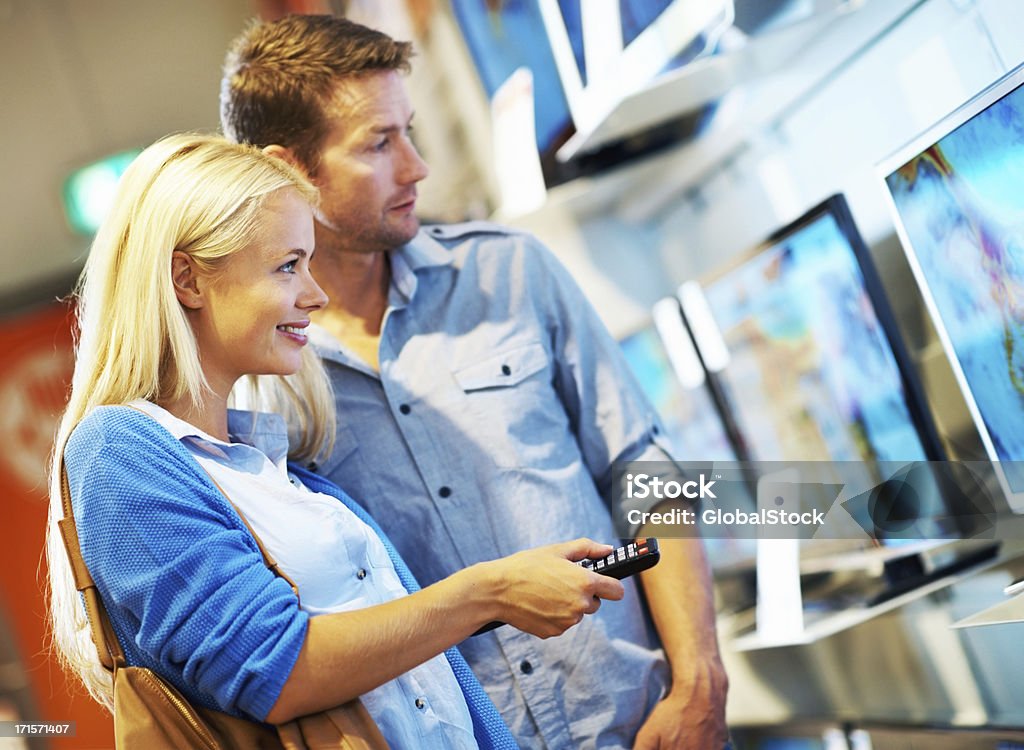 We should go for the LED TV A young couple checking out televisions in an electronic shop Shopping Stock Photo