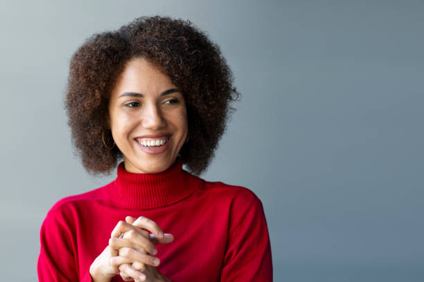 Cheerful African American young woman smiling cutely looking aside, standing over gray wall