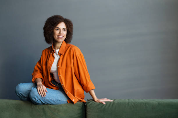 istock Multi-ethnic woman dreamily looking away while relaxing sitting on a couch at home 1715716434