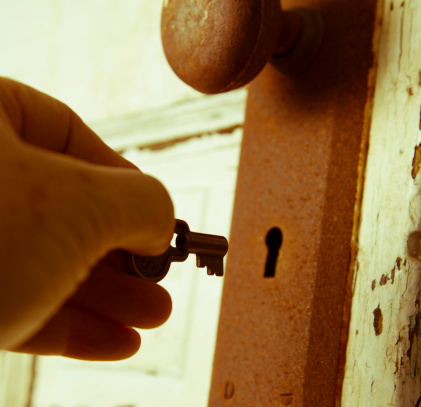 Old rusty door knob on worn door with hand and key unlocking door