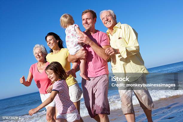 Multi Generation Family Running Along Beach Together Stock Photo - Download Image Now