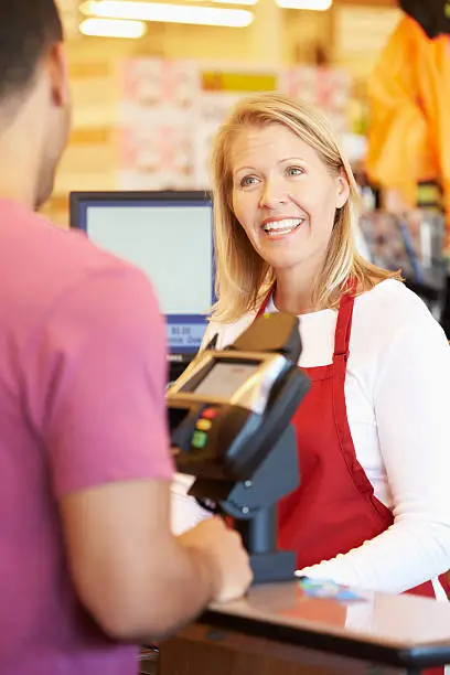 Customer Paying For Shopping At Supermarket Checkout Smiling To Camera