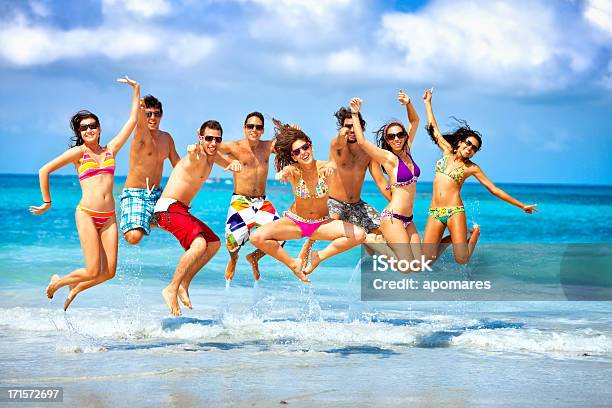 Foto de Feliz Grupo De Jovens Pulando Em Uma Festa De Praia e mais fotos de stock de Festa na praia
