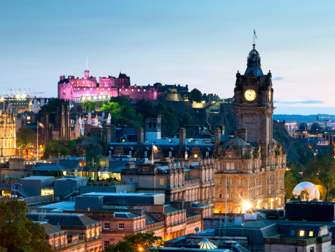 Looking across the city of Edinburgh from Calton Hill at dusk. The Balmoral Hotel and an illuminated Edinburgh Castle can be seen.