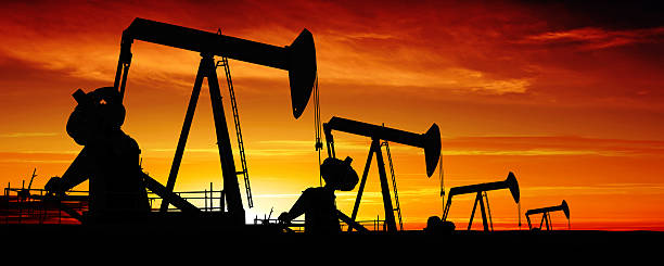 XXXL pumpjack silhouettes oil pumpjacks in silhouette at sunset, panoramic frame (XXXL) oil field stock pictures, royalty-free photos & images