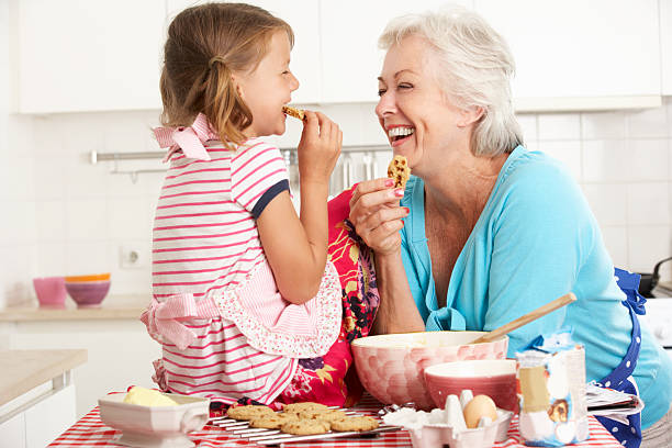 oma und enkelin lachen und gebackene kekse - grandmother cooking baking family stock-fotos und bilder