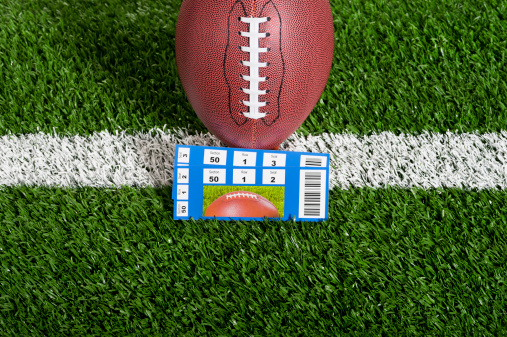 American Football - Tickets, Looking down on pair of ticket stubs in front of a football sitting on a tee over a yard line against artificial turf