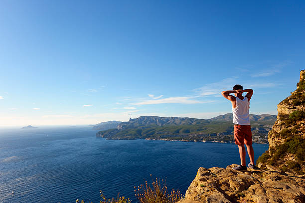 Young man standing on steep cliff at the Cote D'Azur Young man standing on a steep cliff above the sea. Location: Les Calanques, Cassis, French Riviera. casis stock pictures, royalty-free photos & images
