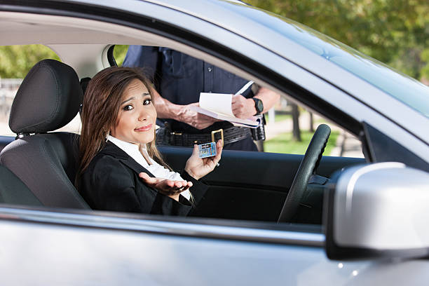 Female Driver Receiving Citation From Police A beautiful young business woman sitting in the drivers seat of her car, holds up her hands and shrugs with hopelessness as a police officer stands outside her vehicle writing her a moving violation ticket. traffic fine stock pictures, royalty-free photos & images