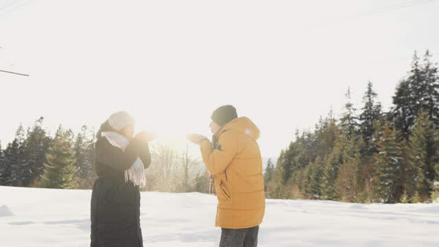 A winter vacation in nature creates an environment where newlyweds can enjoy every moment. They blow snow on top of each other. The couple's fun and smiles reflect the joy of their love,