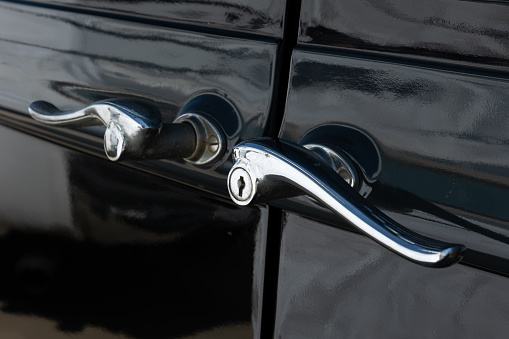A close up of ornate suicide door handles on vintage black car.