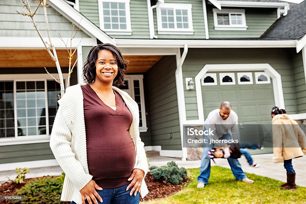 Happy Family of Four at Home Photo of a happy family of four in their front yard; pregnant mother standing in foreground while father plays with daughters in the background. Pregnant Stock Photo