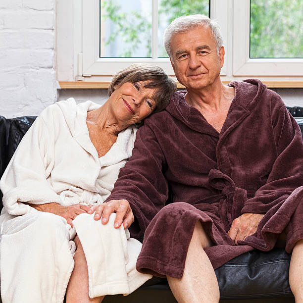 At Ease A senior couple take their time preparing for the day as they relax on the couch after a refreshing night's rest. bathrobe photos stock pictures, royalty-free photos & images