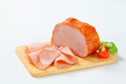 Piece and slices of smoked ham on a cutting board