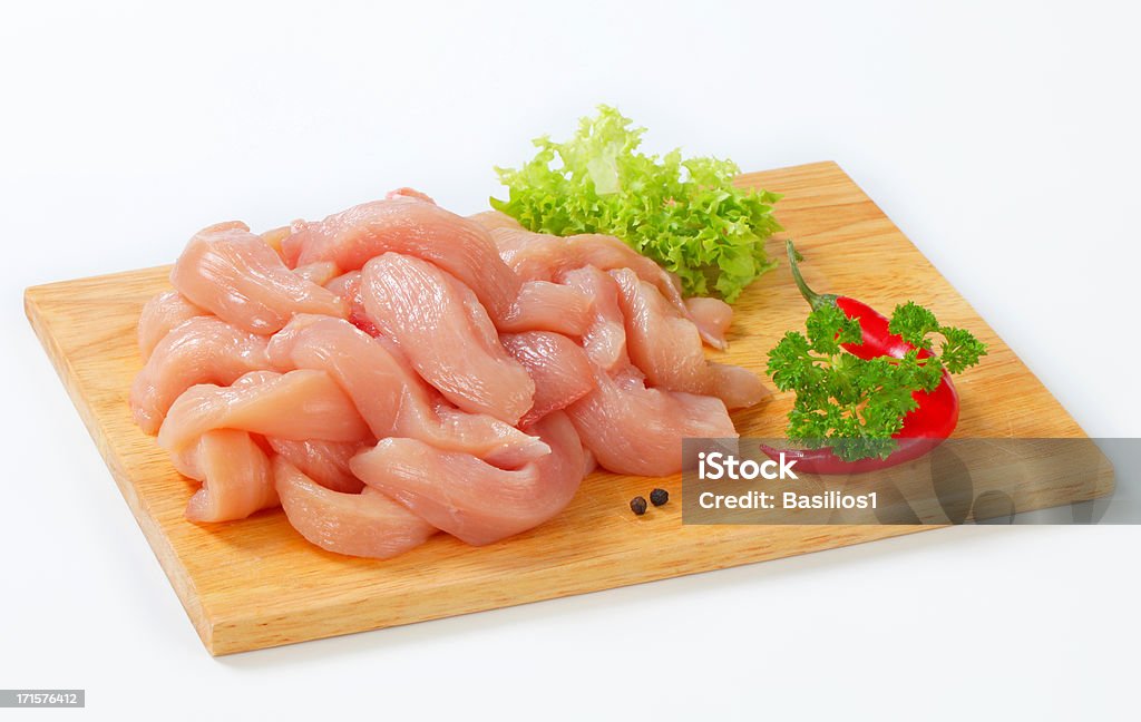 striped raw chicken meat raw chicken meat cut into stripes with vegetables on a wooden cutting board Chicken Meat Stock Photo